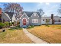 View of charming gray home with a red arched entry door, gray roof, and a traditional lawn with spring color at 2309 Pearl St, Columbus, IN 47201