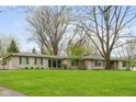 A single-story home with a stone facade and green shutters sits behind a green lawn and mature trees at 7575 Holliday W Dr, Indianapolis, IN 46260