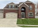 Elegant brick home featuring a prominent arched entryway, three-car garage, and lush green lawn at 11958 Logan Hunter Trl, Noblesville, IN 46060