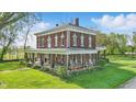 View of brick home with white trim and long front porch, surrounded by green grass and blue skies at 1901 S Old State Road 67, Paragon, IN 46166