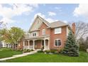 Inviting two-story brick home with a covered front porch and lush green lawn and mature tree at 4777 Madras Ct, Zionsville, IN 46077