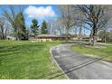 Single-story home with manicured lawn, stone facade, and circular driveway, nestled among mature trees at 1750 W Stop 11 Rd, Indianapolis, IN 46217