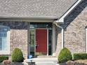 Close up of the front door featuring sidelights, a red door and decorative shrubbery at 8717 Vintner Ct, Indianapolis, IN 46256