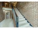 Carpeted staircase with brick wall, iron railing, and a landing featuring a wreath-adorned door at 102 Knoll Ct # D, Noblesville, IN 46062