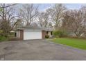 Classic brick home with attached garage and paved driveway, set amongst mature trees at 7026 Spring Mill Rd, Indianapolis, IN 46260