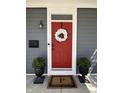 A welcoming red front door with a white wreath and potted plants, set against gray siding with a stylish doormat at 2419 N Park Ave, Indianapolis, IN 46205
