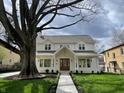 Charming white two-story home with a welcoming front porch, manicured lawn, and a large shade tree at 5940 Central Ave, Indianapolis, IN 46220