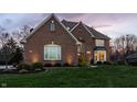 Elegant brick home with a well-kept lawn, manicured landscaping, and warm lighting at dusk at 7326 Elm Ridge Dr, Indianapolis, IN 46236