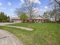 Well-maintained brick ranch home with a three-car garage, beautiful lawn, and mature trees on a sunny day at 2810 Winterway Dr, Shelbyville, IN 46176