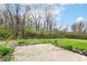 Backyard featuring a brick patio and ample green space with trees in a natural setting at 5856 Long Ridge Pl, Indianapolis, IN 46221