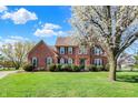 Beautiful two-story brick home with a well-manicured lawn and attractive landscaping and blossoming tree at 11599 Braemar Ct, Carmel, IN 46032