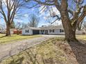 Inviting single-story home with light blue siding, black shutters, a paved driveway, and large mature trees at 1707 W 76Th Pl, Indianapolis, IN 46260