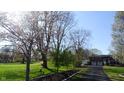 A long driveway leads to a charming two-story brick home with an attached garage, framed by trees and a green lawn at 3790 E Pleasant Run Parkway North Dr, Indianapolis, IN 46201