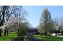 A long driveway leads to a charming two-story brick home with an attached garage, framed by flowering trees and a green lawn at 3790 E Pleasant Run Parkway North Dr, Indianapolis, IN 46201