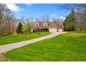 A charming brick home with a three-car garage is showcased with mature trees in the front and winding driveway at 6761 E Woodland Ct, Mooresville, IN 46158