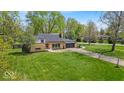 Spacious front yard showcasing a well-maintained lawn, mature trees, and a charming brick home with attached garage at 7205 Steven Ln, Indianapolis, IN 46260