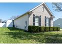 Side view of a brick home with dark shutters, green grass, and an attached shed in the backyard at 122 Stamford Dr, Pittsboro, IN 46167