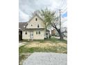 View of the two-story home with yellow siding, large yard and detached gravel parking space at 3502 N Illinois St, Indianapolis, IN 46208