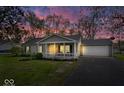 Charming single-story home with a well-manicured lawn, cozy porch, and attached garage at sunset at 7709 Lewis Rd, Indianapolis, IN 46256