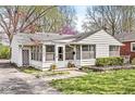 Quaint home boasts an enclosed porch, large windows, and is surrounded by blossoming trees and a green lawn at 6153 Evanston Ave, Indianapolis, IN 46220
