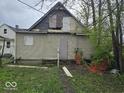 Rear exterior view of a distressed property showing siding damage, boarded windows and overgrown weeds at 727 W 25Th St, Indianapolis, IN 46208