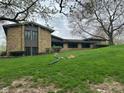 View of the back of the home with a stone facade, grassy slope to the back and mature trees at 8801 Ridge Hill Dr, Indianapolis, IN 46217