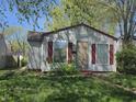 Exterior view of a single-story home with gray siding, red trim, and partially boarded windows at 1138 N Exeter Ave, Indianapolis, IN 46222