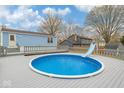 Backyard featuring an above-ground pool with a slide, surrounded by a spacious deck and mature trees at 11423 Mutz Cir, Indianapolis, IN 46229