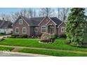 Lovely brick home features well-maintained lawn, mature landscaping, and charming architectural details at 5861 Dawnwood Dr, Carmel, IN 46033