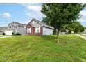 A grassy yard is shown in this charming home's exterior, framed by a large tree at 6479 Enclave Blvd, Greenwood, IN 46143