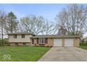 Well-kept split-level home features a two-car garage and a large front yard landscaped with mature trees at 7171 N Orchard Dr, Indianapolis, IN 46236