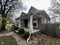 A quaint home featuring a covered porch, wooden fence, and mature trees in a serene setting at 1626 S State Ave, Indianapolis, IN 46203