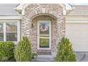 Close-up of a charming front door with a decorative wreath, brick archway, and manicured shrubbery at 47 Thornburg Pkwy, Brownsburg, IN 46112