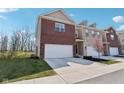 Two-story townhome featuring an attached garage, brick facade, and landscaped front yard under a bright sunny sky at 9725 Thorne Cliff Way # 105, Fishers, IN 46037