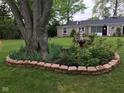 Beautifully landscaped front yard features a large tree and vibrant flower bed, with a charming home exterior in background at 3155 W 57Th St, Indianapolis, IN 46228
