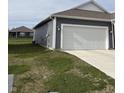 Exterior view showcasing a spacious two-car garage with gray siding, complemented by manicured lawn and surrounding greenery at 1380 Fairmount Dr, Greenfield, IN 46140