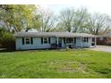 A light blue single-story home with a well-manicured lawn, mature trees, and a paved driveway at 10360 Wilson Rd, Brownsburg, IN 46112