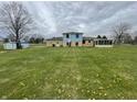 Large backyard with green lawn, dandelions and the back of the light blue and tan home at 1387 W Furry Rd, Fountaintown, IN 46130