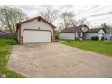 View of the house featuring a two-car garage with neutral siding, brick accents, and a long concrete driveway at 9143 Warwick Rd, Indianapolis, IN 46240