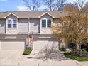 Inviting townhouse featuring an attached garage, mature landscaping, and a charming American flag at 11264 Fonthill Dr, Indianapolis, IN 46236