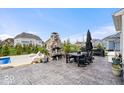 Outdoor living space featuring stone fireplace, patio dining set, grill, lush landscaping, and a glimpse of the pool at 1352 Trifecta Way, Westfield, IN 46074