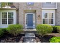 Welcoming front entrance with well-manicured bushes, blue door, and brick facade at 14323 Chariots Whisper Dr, Carmel, IN 46074