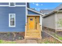 Inviting yellow front door with wooden steps, set against a blue-sided home and landscaped garden bed at 614 Park Ave, Anderson, IN 46012