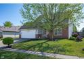 Charming home with a lush green lawn, mature tree, brick accents, and an attached two car garage at 419 Old Glory Dr, Greenfield, IN 46140