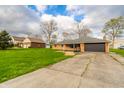 This single-story brick home includes a two-car garage and cracked driveway at 5576 N Heritage Ln, Alexandria, IN 46001