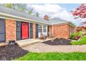 Inviting front porch with a red door, black shutters, and chairs, complemented by neat landscaping at 7756 N Audubon Rd, Indianapolis, IN 46250