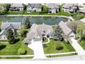 Aerial view of a home showing the backyard pond, green lawn, mature trees, and three car garage at 11862 Stoney Bay Cir, Carmel, IN 46033