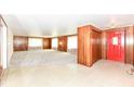 Spacious living room featuring wood-paneled walls, plush carpeting, and a bright red front door at 830 N 16Th St, Elwood, IN 46036