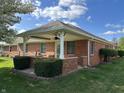 Brick home exterior view of covered back patio with ceiling fan and manicured shrubbery at 379 Vinewood N Dr, Brownsburg, IN 46112