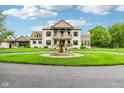 Elegant two-story home with a circular driveway, fountain, manicured lawn, and classic architectural details at 6990 Old Hunt Club Rd, Zionsville, IN 46077